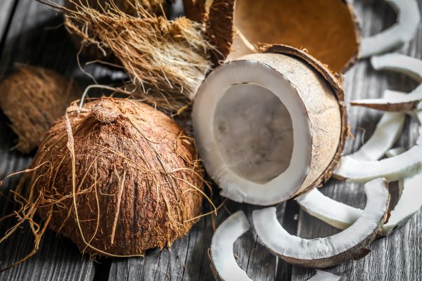 Fresh coconuts broken on wooden background with coconut milk in small glass jars